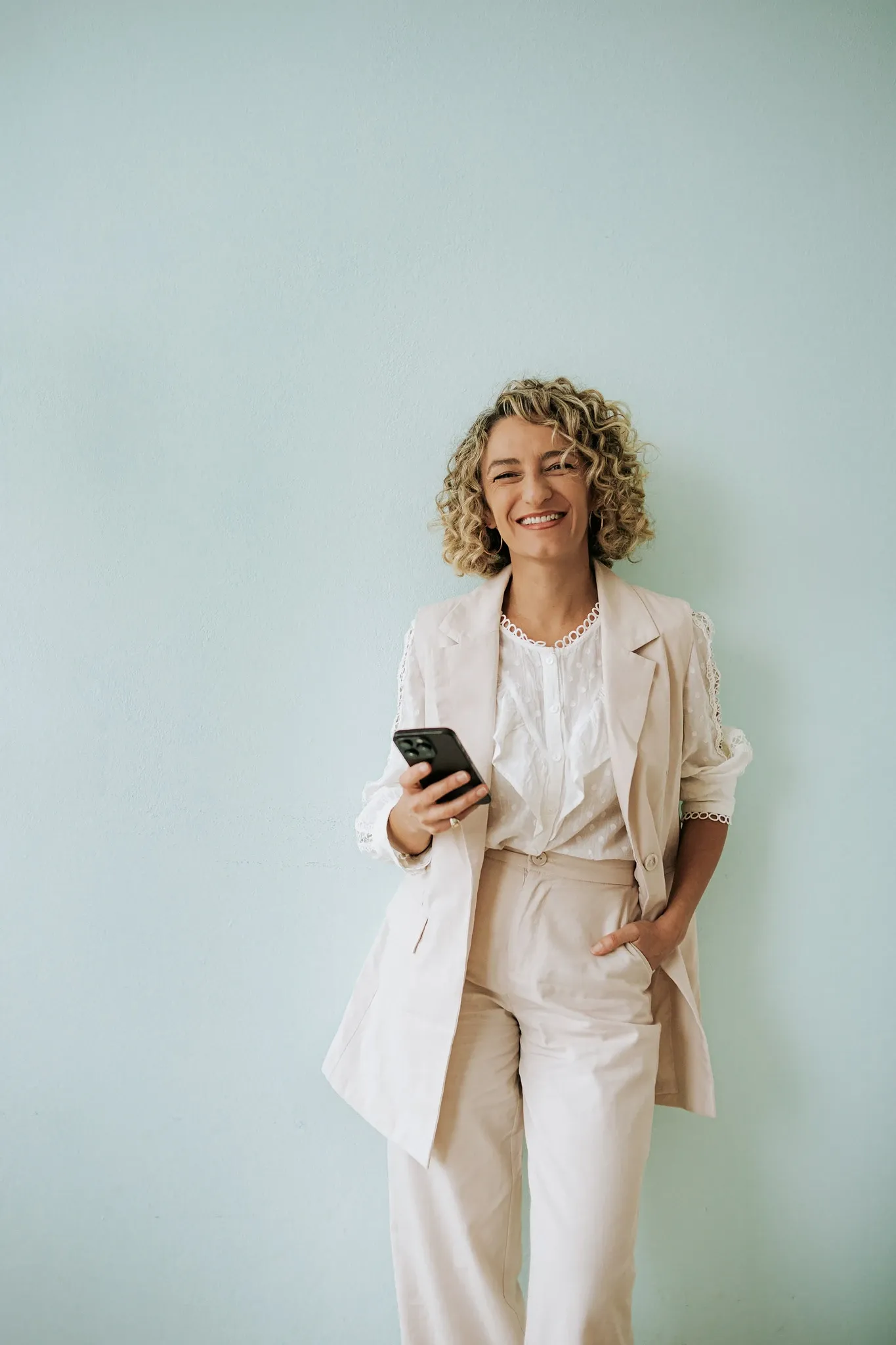 Daniela Pérez sonriendo, con un traje claro y el celular en la mano.